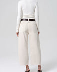 Person wearing a white long-sleeve top and cream-colored wide-leg pants on a white background