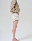 Person wearing a beige jacket and floral skirt on a plain background