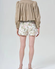 Person wearing a beige shirt and floral shorts on a white background