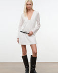 Woman wearing a white dress and black knee-high boots against a plain background