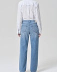Person wearing a white shirt and light blue jeans on a plain background