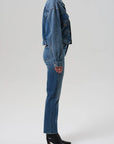 Person wearing a blue denim jacket and jeans on a white background side view