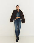 Person wearing a dark brown coat, denim jacket, and jeans standing against a white background front view