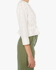 Woman wearing a white blouse and green pants on a white background, side