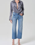 Person wearing a gray button-up shirt and blue jeans on a light gray background