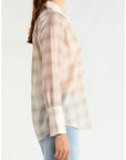 A woman shown in side profile wearing a sheer, long-sleeve button-up shirt with a beige and white plaid pattern, paired with light blue jeans, against a plain white background.
