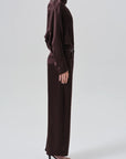 A model shown from the side wearing a dark brown satin turtleneck top and matching wide-leg trousers with a tie belt at the waist, paired with black high-heeled sandals, against a light gray studio background.