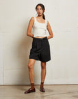 Woman wearing a white tank top and black shorts against a plain wall front view