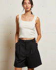 Woman wearing a white tank top and black shorts against a plain background front view