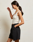 Woman wearing a white tank top and black skirt against a plain background side view