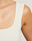 Close-up of a person wearing a white tank top against a neutral background detail view