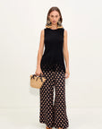 Woman wearing a black sleeveless top and polka dot pants, holding a woven bag on a white background
