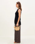 Woman holding a straw bag, wearing a black sleeveless top and patterned pants on a white background