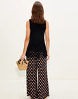 Woman wearing a black sleeveless top and patterned pants, holding a straw bag on a white background