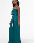 Woman wearing a teal strapless jumpsuit on a white background