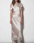 A woman models a champagne satin off-the-shoulder midi skirt with a lace hem, standing against a plain white studio wall.