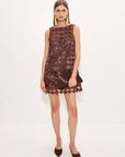 A model wearing a sleeveless brown crochet lace mini dress with a scalloped hem and matching pointed-toe flats, standing against a plain white studio background.