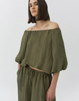 Woman wearing an off-shoulder green top and high-waisted pants on a white background