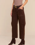 A model wearing dark brown wide-leg cropped pants with a matching dark brown belt featuring a gold buckle, styled with a mauve top and dark brown heeled ankle boots against a solid beige studio background.
