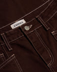 Close-up of dark brown corduroy pants showing the waistband, belt loops, button, and white contrast stitching. A white fabric label reading 'L'AGENCE' is visible near the waistband.