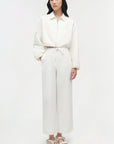 Person wearing a white outfit with straight-leg pants on a plain background
