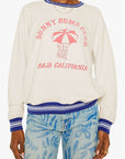 Person wearing a white sweatshirt with 'Sunny Bums Club' text and graphics, paired with blue pants.