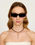 Woman wearing black sunglasses, gold earrings, and a brown leather necklace on a white background