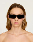 Woman wearing black sunglasses and gold earrings against a white background