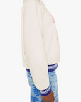 Person wearing a cream sweatshirt with colorful accents and blue patterned pants on a white background, side view