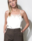 Woman wearing a white lace top and brown pants against a white background