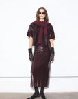 Model wearing a burgundy sequin outfit with sunglasses and gloves against a white background