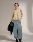A model stands in a studio wearing a sleeveless cream shaggy top, light blue wide-leg pants, and dark brown heeled boots, while holding a black jacket against a plain light background.
