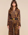 A woman modeling a leopard-print long-sleeve collared set with a black belt featuring a gold buckle, set against a solid beige background.