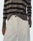Person wearing a gray and black striped long-sleeve shirt with white pants on a light gray background