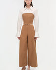 Woman wearing a white blouse and brown high-waisted pants on a white background