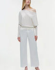 Woman wearing a white off-shoulder top and white pants on a white, background, full body