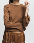 Person wearing a brown sweater and plaid skirt on a white background