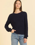 Woman wearing a navy sweater and blue jeans against a beige background