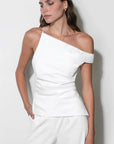 A woman modeling a white off-the-shoulder wrap top with matching white wide-leg trousers, standing against a plain light gray wall.