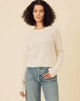 Woman wearing a white sweater and blue jeans against a beige background