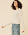 Woman wearing a white sweater and blue jeans against a beige background