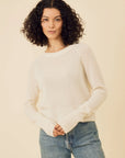 Woman wearing a beige sweater and blue jeans against a beige background