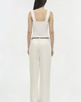 Woman wearing a white sleeveless top and pants on a white background back view