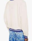 Person wearing a cream sweater with blue trim and blue floral pants on a white background