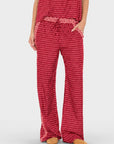 A person wearing red and white patterned lounge pants with a matching drawstring belt and a matching red top, standing against a light gray studio background.