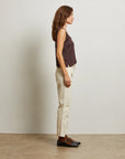 Woman standing against a plain wall wearing a sleeveless top, beige pants, and brown shoes side view