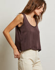 Woman wearing a brown tank top and beige pants against a plain background side view