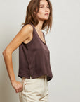 Woman wearing a sleeveless brown top and beige pants against a plain background side view
