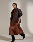 Woman wearing a brown leather jacket and dress with black boots against a neutral background