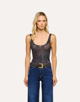 A blonde model stands against a light gray studio background wearing a dark patterned sleeveless bodysuit with blue jeans and a brown belt.